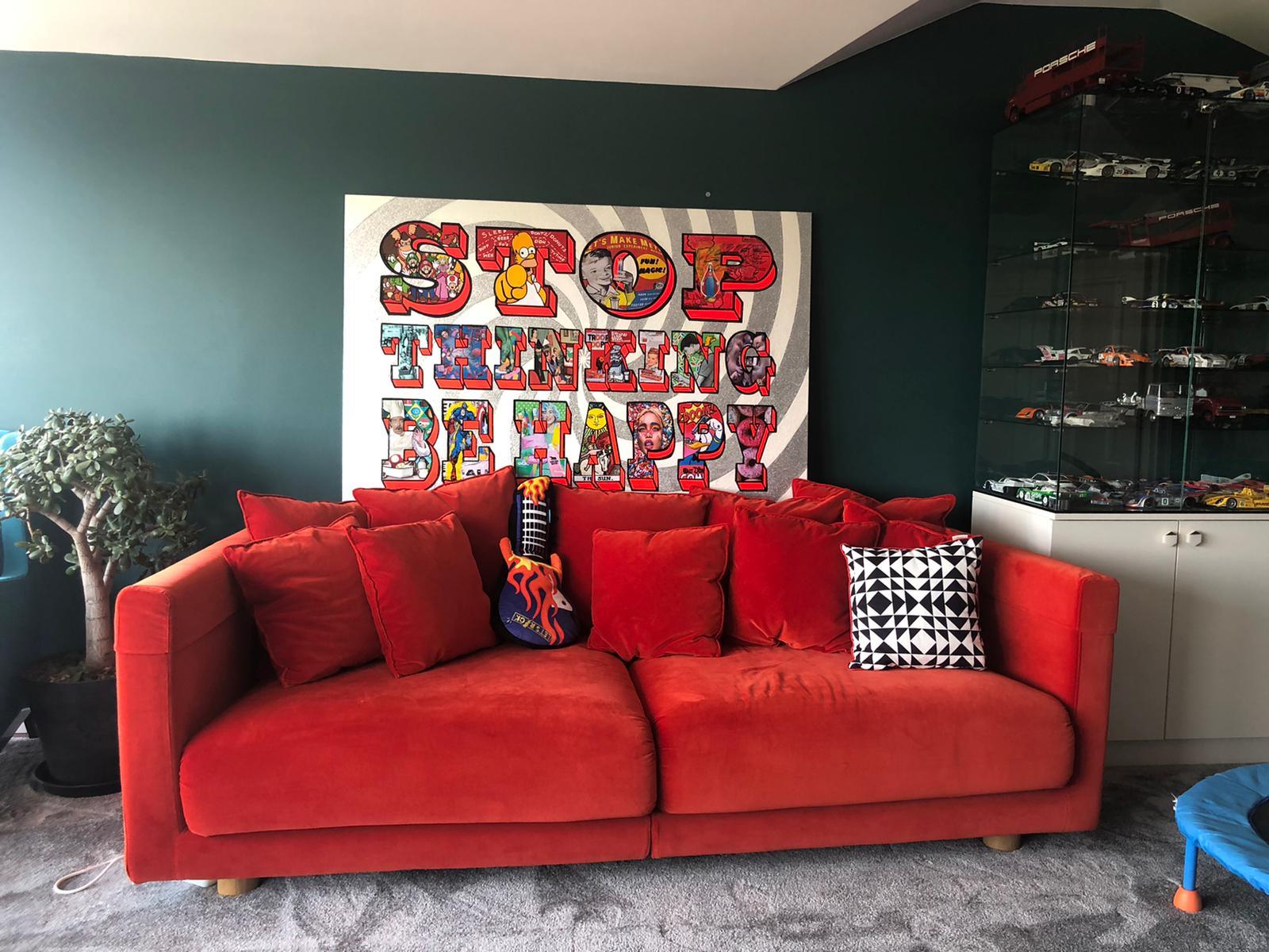 Bright red sofa with cushions and a flame guitar pillow in living room with colorful 'Stop Thinking Be Happy' wall art
