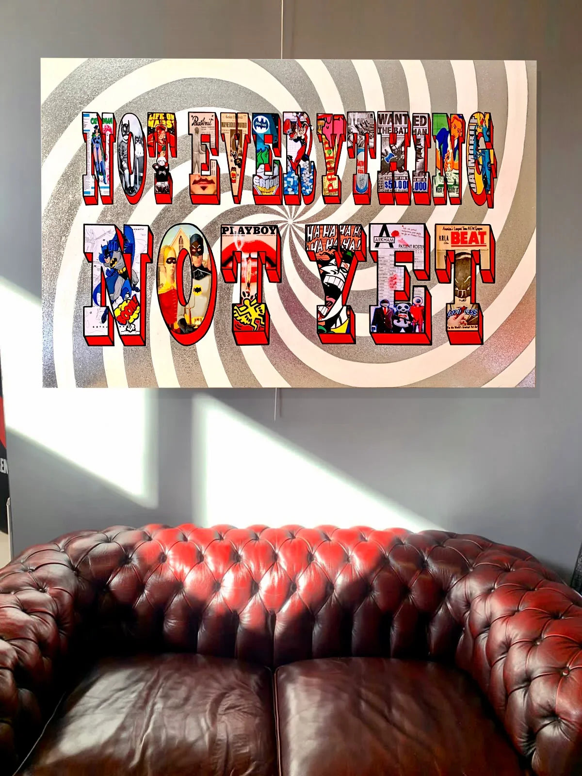 Colorful pop art wall sign with text 'NOT EVERYTHING NOT SHT' above a red leather tufted sofa